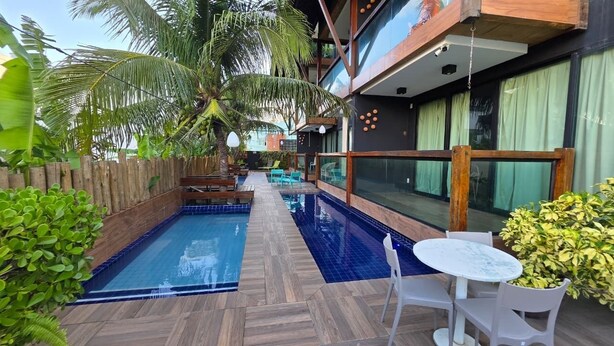A pool area with wooden decking, lounge chairs, and a table. - Merepe Suites 103 by La Playa (Ipojuca)