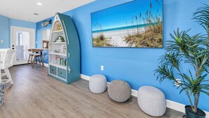 Ein Zimmer mit blauer Wand, einem Strandbild, einem weißen Schrank und einer Topfpflanze.