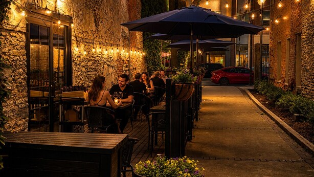 An outdoor dining area with stone walls, tables, chairs, and string lights.