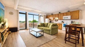 A modern living room with a green sofa, a coffee table, and a dining area with wooden chairs.