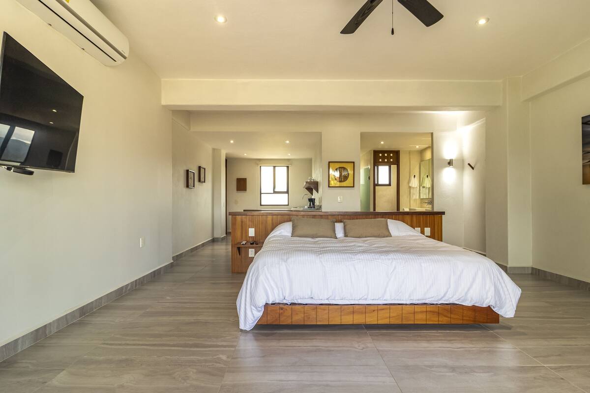 Een slaapkamer met een groot bed, een aan de muur bevestigde televisie en een plafondventilator.