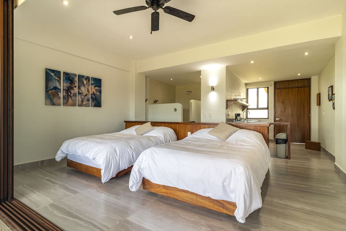 Een slaapkamer met twee bedden, een plafondventilator, een bureau en een zichtbare badkamer door een open deur.