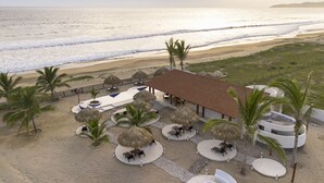 Un complexe hôtelier situé en bord de mer, doté d’une piscine, de chaises longues et de palmiers.