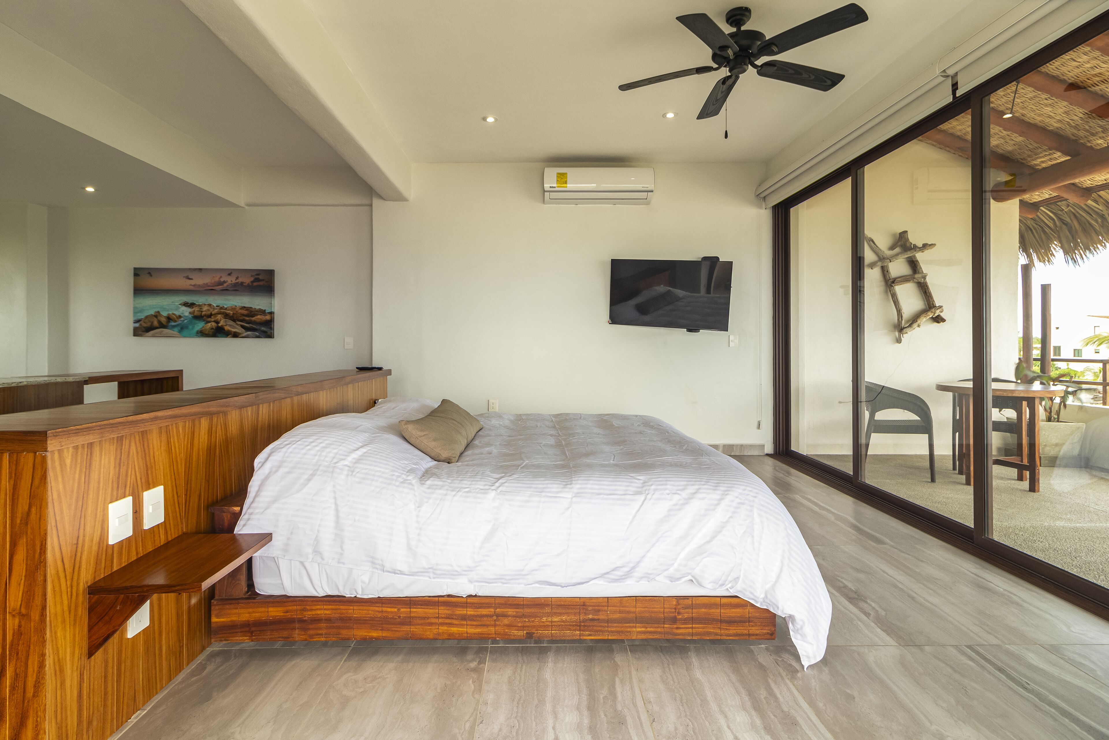 Un dormitorio con una cama grande, un ventilador de techo, un equipo de aire acondicionado, un televisor y un ventanal con vistas al exterior.