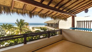 Un balcon avec vue sur la plage et l’océan, un toit de chaume et une balustrade.
