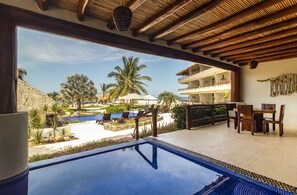 A poolside area with a view of a resort, including a pool, lounge chairs, and a dining area.