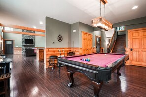 A pool table with a red felt surface, wooden walls, a stone fireplace, and a staircase. - Starr & Sky Lodge | Hocking Hills, Hot Tub, Sauna (Logan)