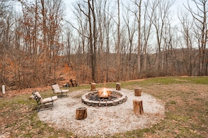 A circular fire pit surrounded by wooden stumps and two lounge chairs in a wooded area. - Starr & Sky Lodge | Hocking Hills, Hot Tub, Sauna (Logan)