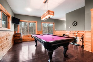 A pool table in a room with wooden walls, large windows, and a ceiling light fixture. - Starr & Sky Lodge | Hocking Hills, Hot Tub, Sauna (Logan)