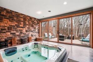 A spa area with a hot tub, stone wall, and a view of a patio with outdoor furniture. - Starr & Sky Lodge | Hocking Hills, Hot Tub, Sauna (Logan)