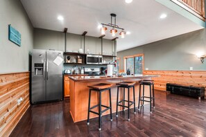 A kitchen with a central island, bar stools, stainless steel appliances, and wooden paneling. - Starr & Sky Lodge | Hocking Hills, Hot Tub, Sauna (Logan)
