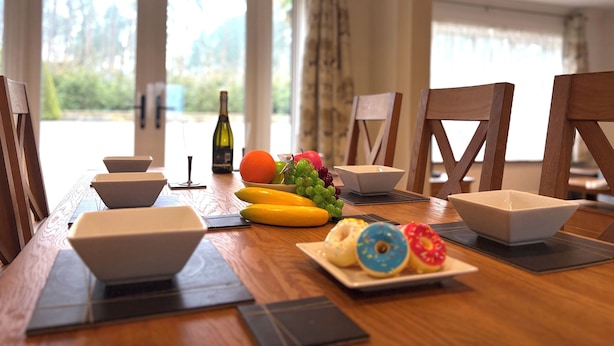 Une table à manger avec une bouteille, des fruits et une assiette de beignets.