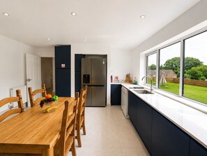 Uma cozinha moderna com uma mesa de jantar, cadeiras, uma geladeira e uma grande janela com vista para o exterior.