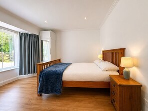 A bedroom with a bed, bedside lamps, a wooden nightstand, and a window with curtains. - Spacious Cotswolds Home-Large Garden-Games Room (Finstock)