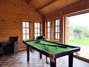 Une table de billard recouverte d’un drap vert, avec des parois en bois et de grandes fenêtres.