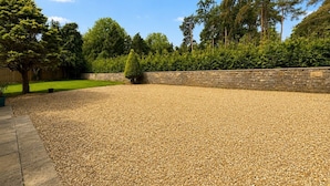 A gravel driveway leading to a stone wall with a hedge and trees in the background. - Spacious Cotswolds Home-Large Garden-Games Room (Finstock)