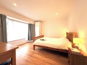 Une chambre avec un lit en bois, une table de chevet avec une lampe, une fenêtre avec des rideaux et un système de climatisation intégré.
