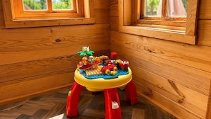 A wooden cabin interior with a children's play area featuring a colorful LEGO table and a small stool. - Spacious Cotswolds Home-Large Garden-Games Room (Finstock)