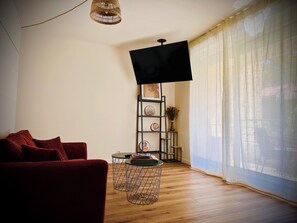 Ein Wohnzimmer mit einem roten Sofa, einem Fernseher auf einem Schrank, einem kleinen runden Tisch und einem Bücherregal.