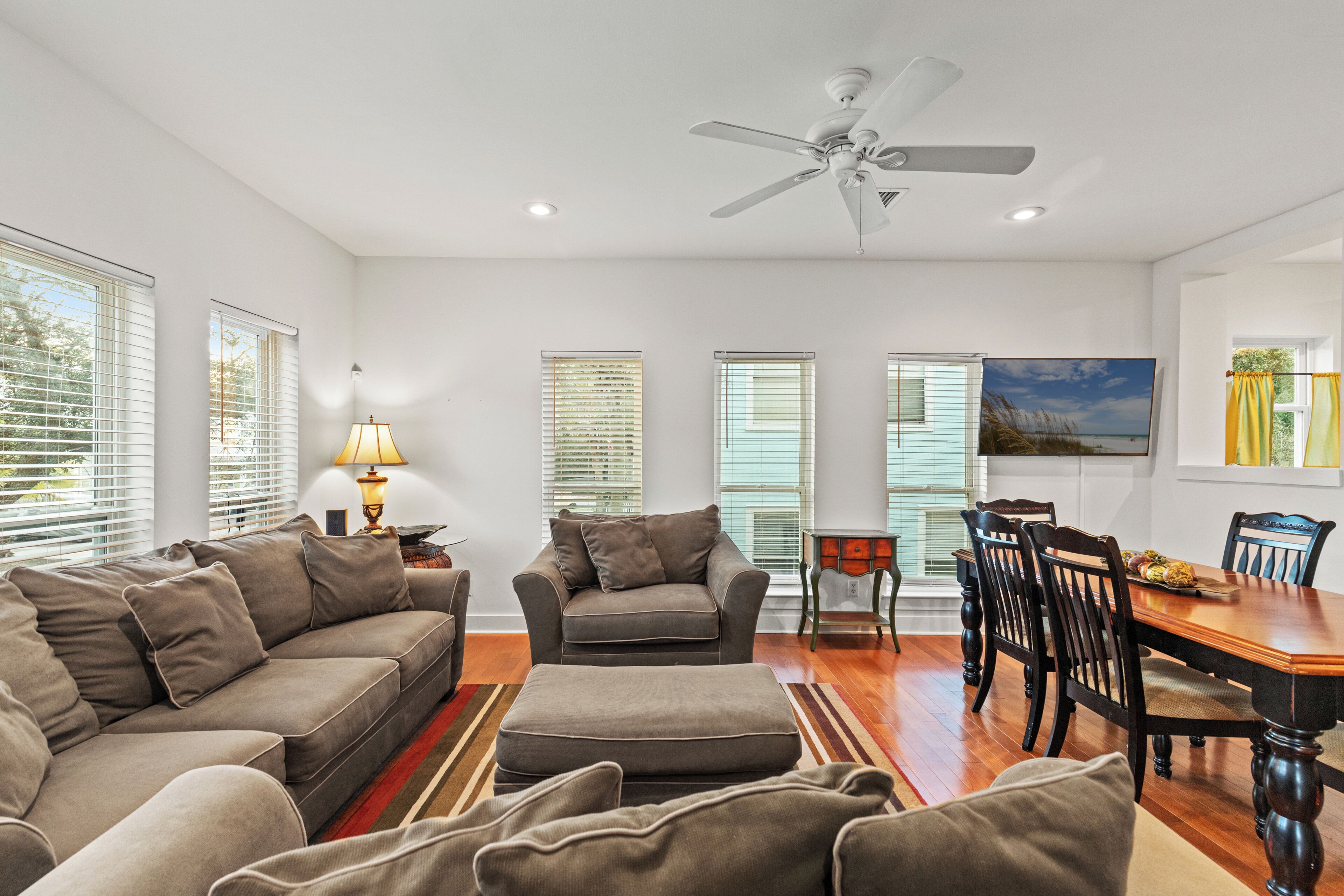 A living room with a sofa, armchair, ottoman, dining table with chairs, and a ceiling fan.
