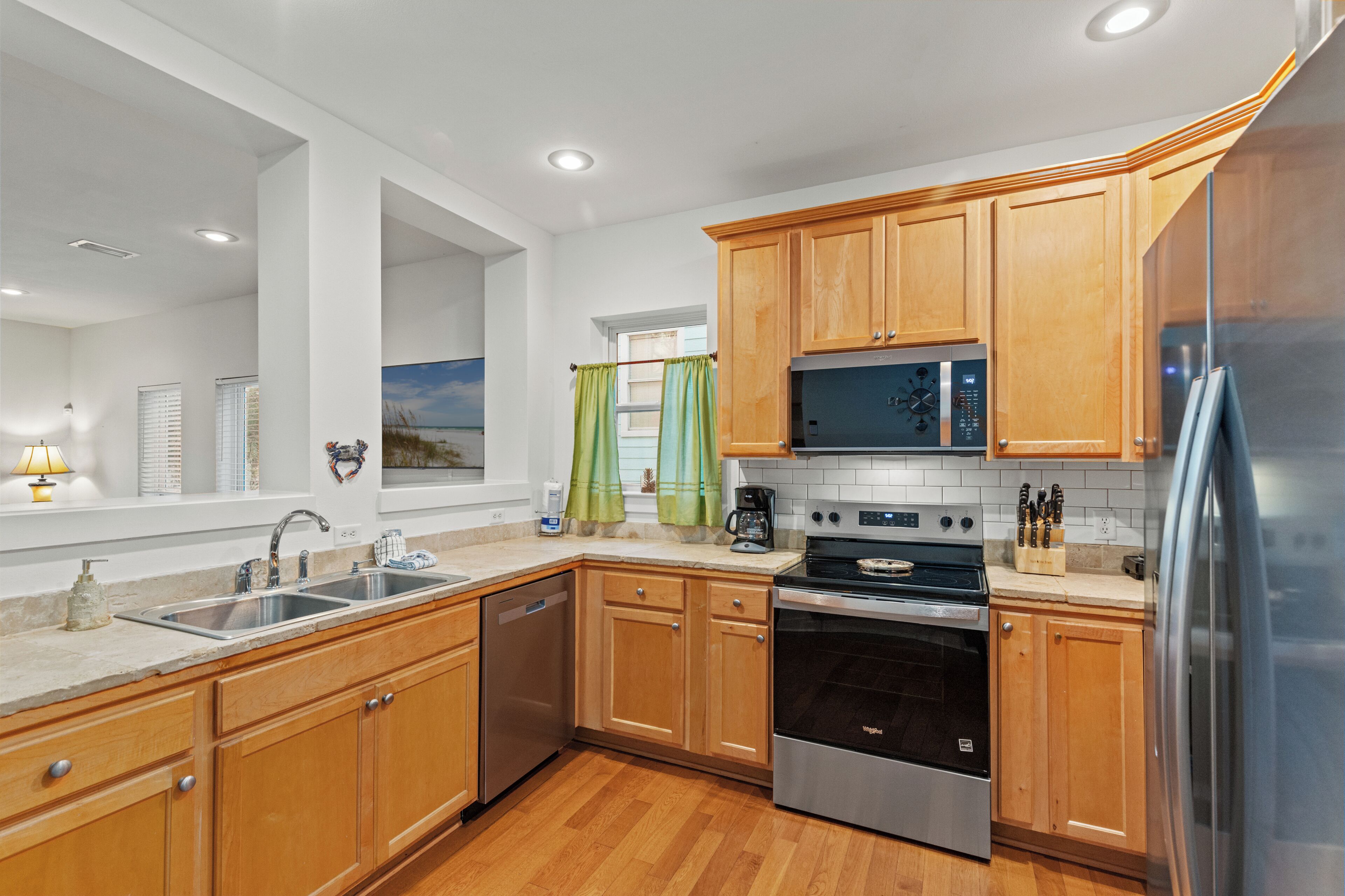 A modern kitchen with wooden cabinets, stainless steel appliances, and a window with curtains.