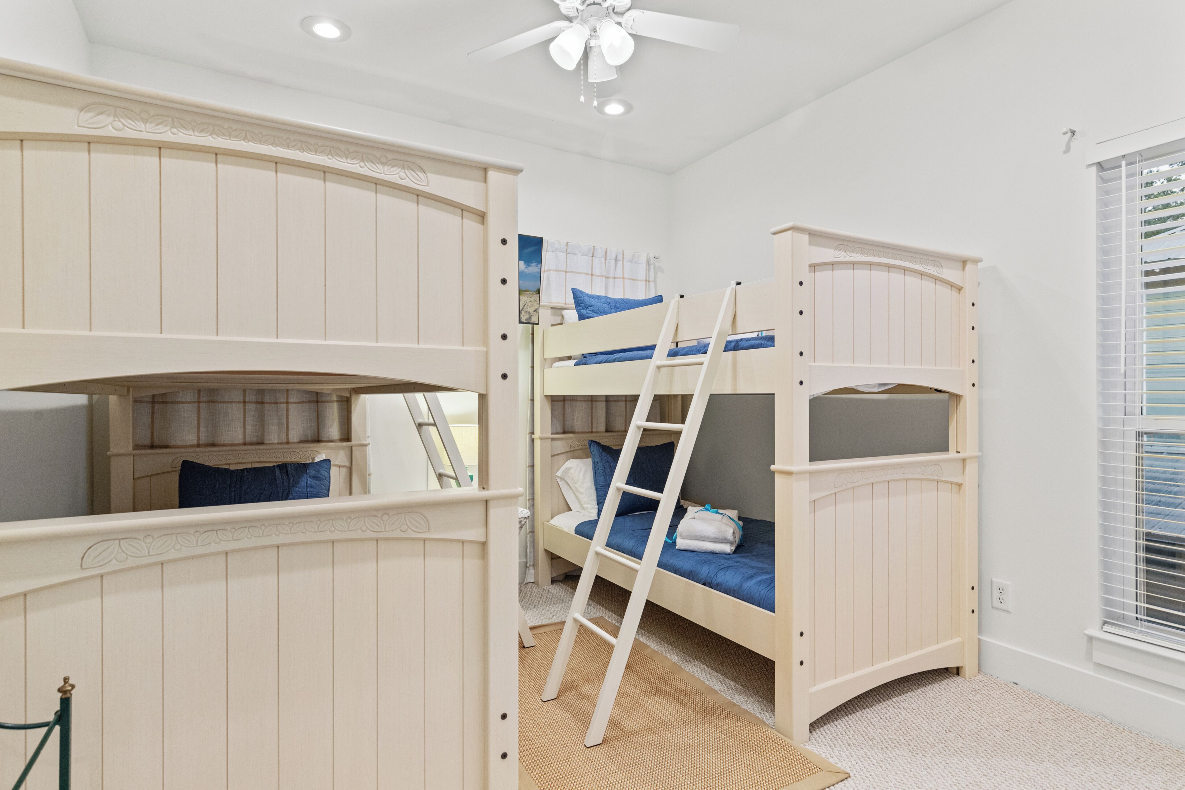 A bunk bed room with a ladder, a window with blinds, and a ceiling fan.