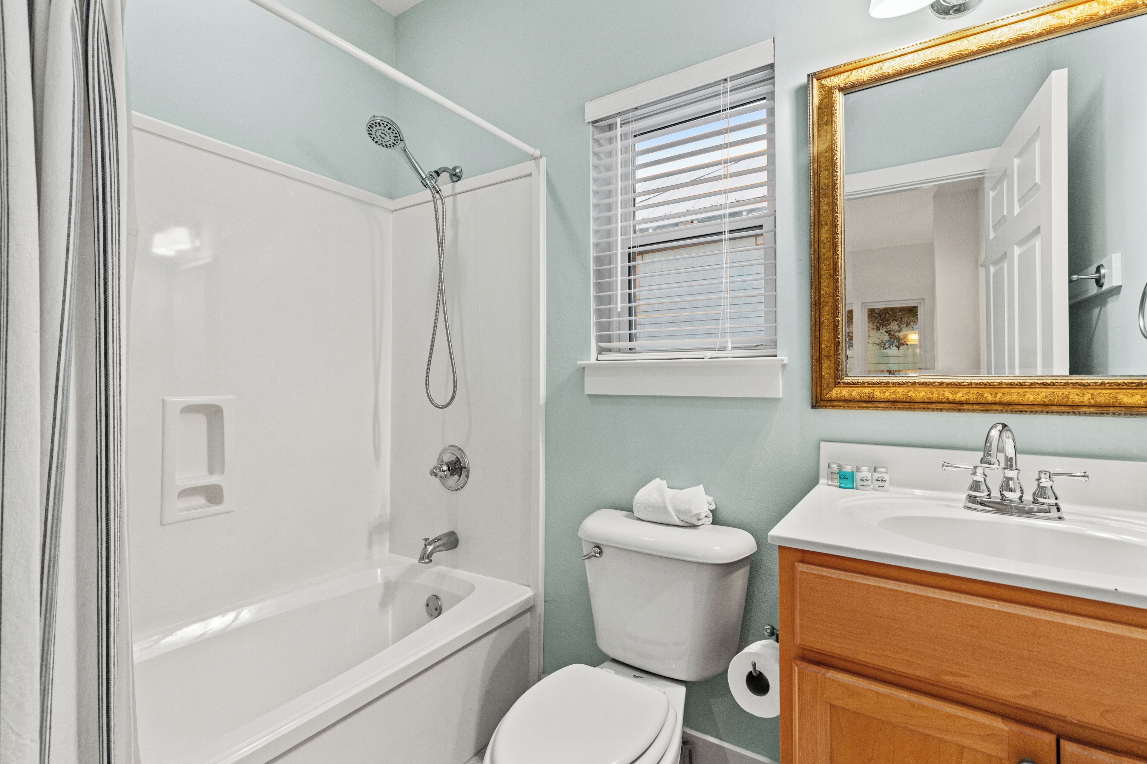 A bathroom with a shower, toilet, sink, and mirror.