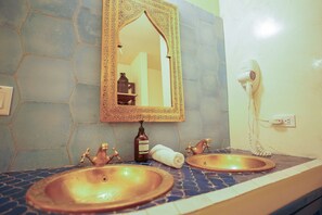 Un baño con dos lavamanos, un espejo, un secador de pelo y una botella de jabón de manos.