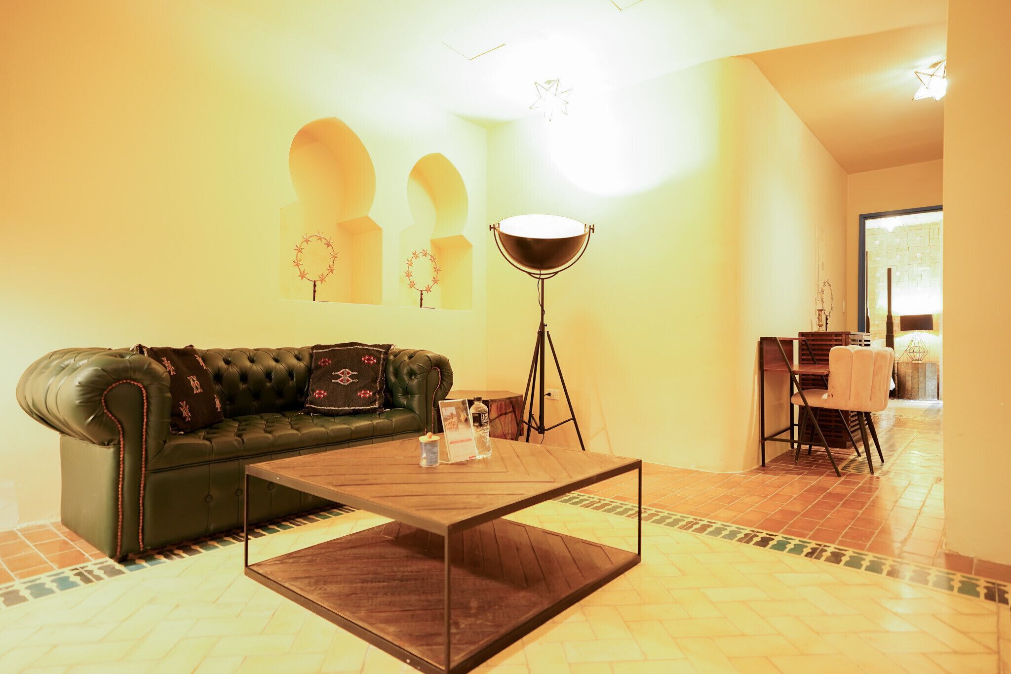 A living room with a green leather sofa, a wooden coffee table, a floor lamp, and a dining area with a table and chairs.
