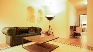 A living room with a green leather sofa, a wooden coffee table, a floor lamp, and a dining area with a table and chairs.