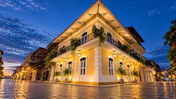 A hotel with a classic architectural style, featuring a central courtyard, multiple balconies with plants, and a warm, inviting atmosphere.