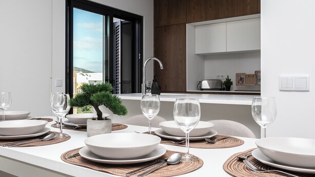 A modern kitchen with white countertops, a built-in oven, and a window with a view of the city. - Serena By Marenssa (Moncarapacho)