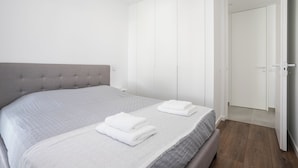 A modern bedroom with a large bed, a grey upholstered headboard, and a wardrobe with sliding doors. - Serena By Marenssa (Moncarapacho)