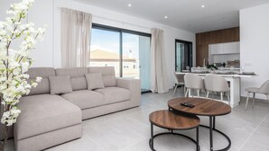 A modern living room with a sofa, a dining table, and a kitchen area with a counter and chairs. - Serena By Marenssa (Moncarapacho)