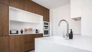 A modern kitchen with wooden cabinets, a white countertop, a sink with a faucet, and built-in appliances. - Serena By Marenssa (Moncarapacho)