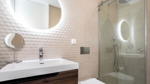 A modern bathroom with a white sink, a mirror, a toilet, and a glass-enclosed shower area. - Serena By Marenssa (Moncarapacho)