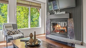 A modern living room with a fireplace, large windows, a comfortable chair, and a decorative table. - Chic Rocky Mountain 2BR w/ Hot tub and Pool (Canmore)