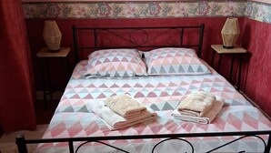 Een bed met een gebedekte spreideken, twee kussens en twee opgevouwen handdoeken. Er staan twee nachtkastjes met lampen.