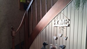Een trap met een 'HOME' bord, een klein tafeltje met decoratieve objecten, en een geruite vloer.