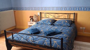 Een slaapkamer met een metalen bedframe, een blauw bed met een patroon en een klein nachtkastje met een lamp.