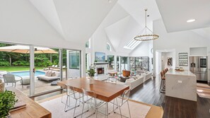 A spacious living area with a large wooden dining table, a fireplace, and a view of a swimming pool. - Modern East Hampton Retreat, Exquisitely Appointed with a Private Pool,... (East Hampton)