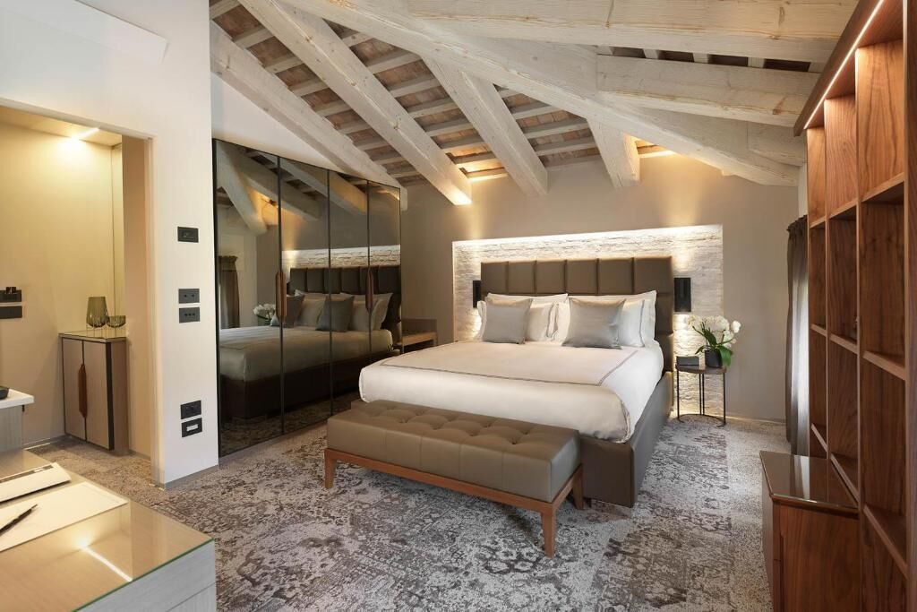 A bedroom with a large bed, a bench, a wardrobe, and a mirror.