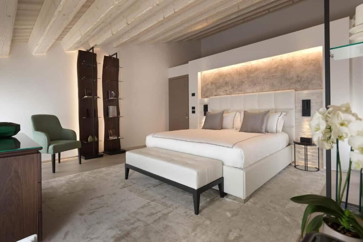 Ein modernes Schlafzimmer mit einem großen Bett, einem grünen Sessel, einem Holzregal und einem kleinen Nachttisch.