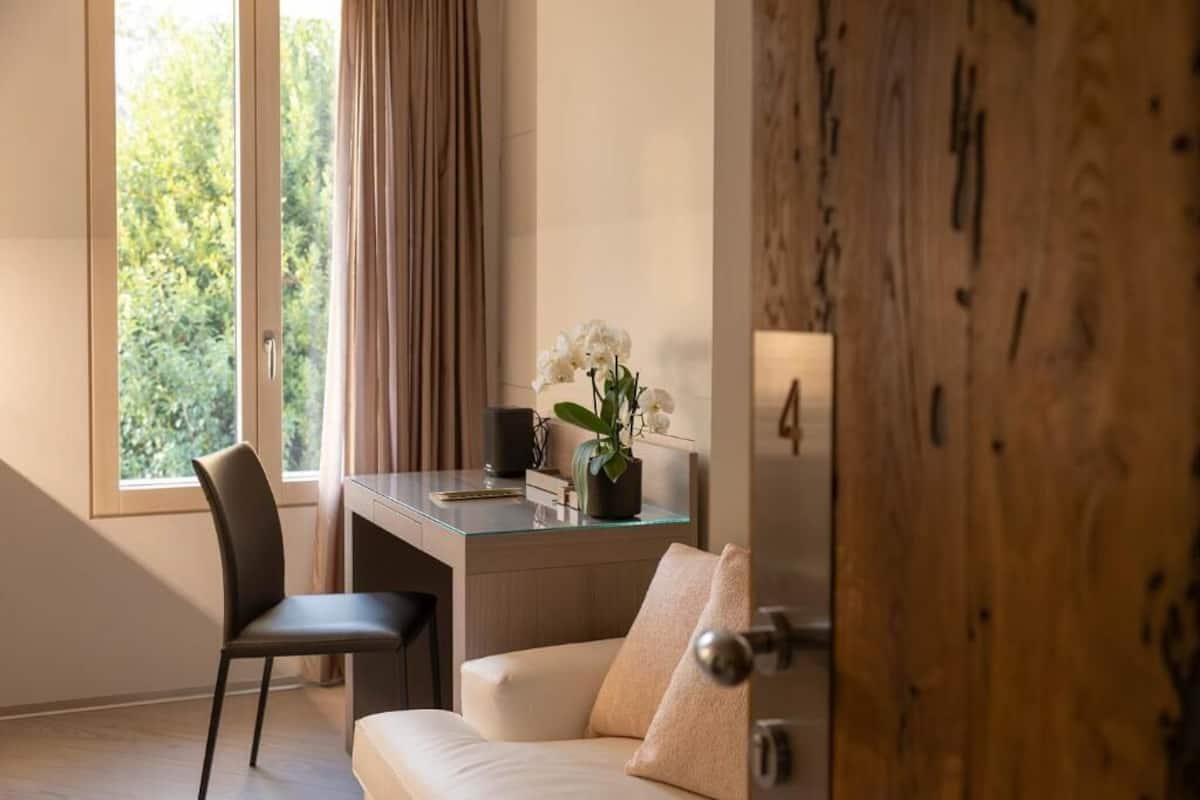Ein modernes Zimmer mit Schreibtisch, Stuhl, Sofa und Blick ins Grüne durch ein Fenster.