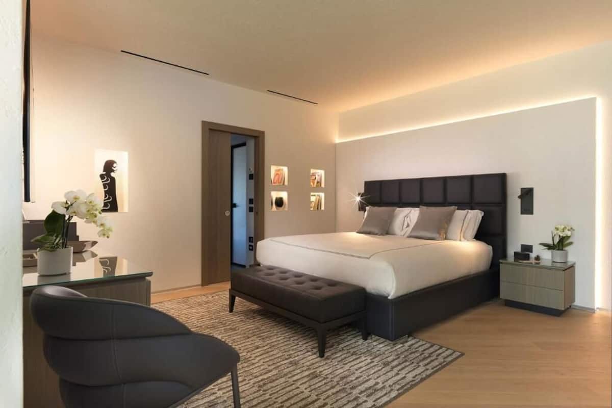 Ein modernes Schlafzimmer mit einem großen Bett, einem Nachttisch, einem Sessel und einem kleinen Schreibtisch.