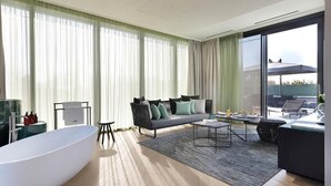 Une salle de bain moderne avec une baignoire sur pieds, un canapé avec des coussins, une table basse et une vue sur un balcon.