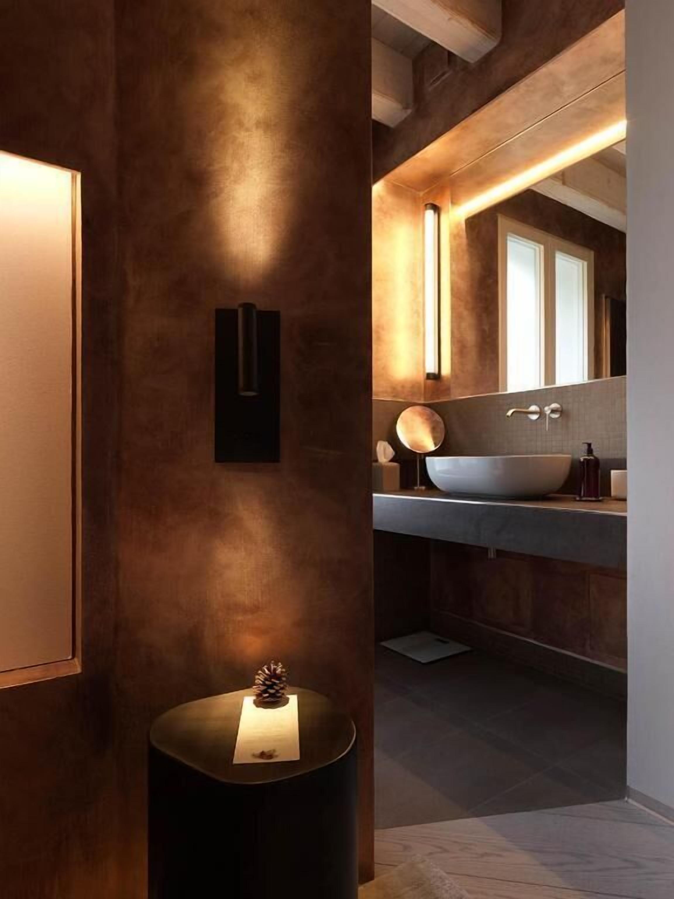 Un baño moderno con un espejo grande, un lavabo redondo y una lámpara de pared.