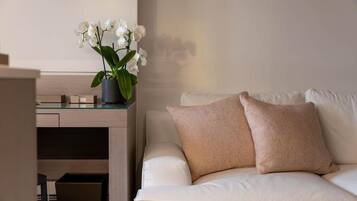 Una sala de estar moderna con un sofá blanco, dos cojines color beige, una mesa de centro de vidrio y una orquídea blanca en maceta.