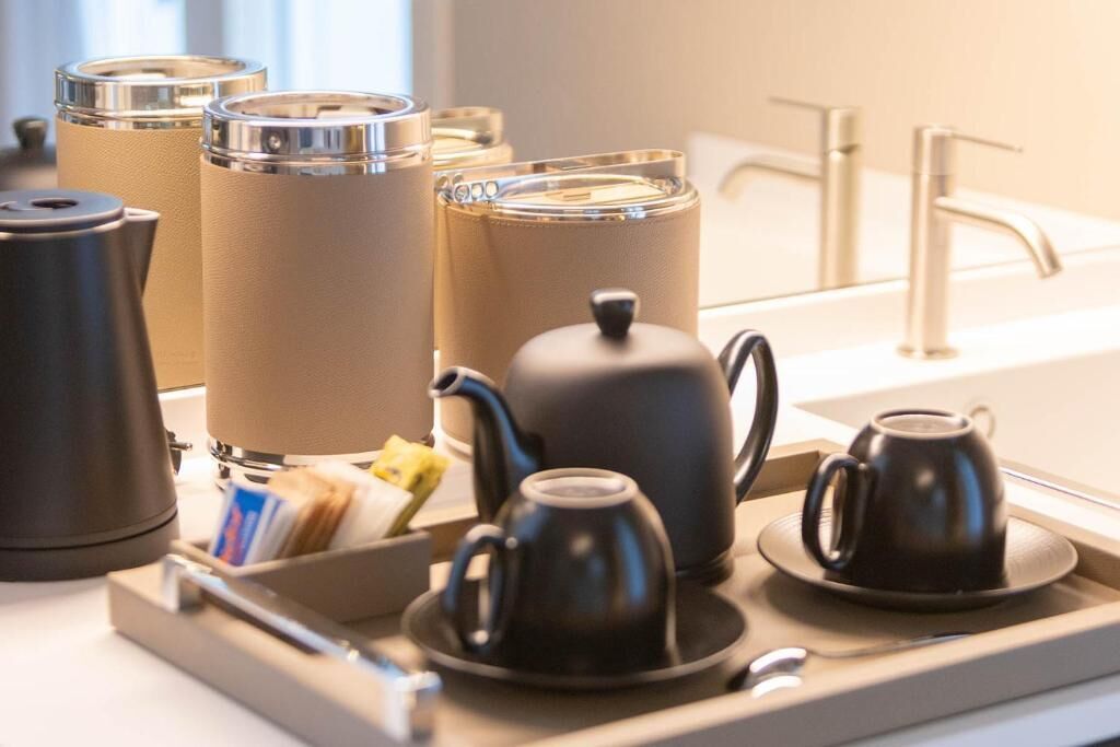 Una bandeja con un juego de té, que incluye una tetera, tazas y un azucarero, junto con una cafetera y un hervidor.