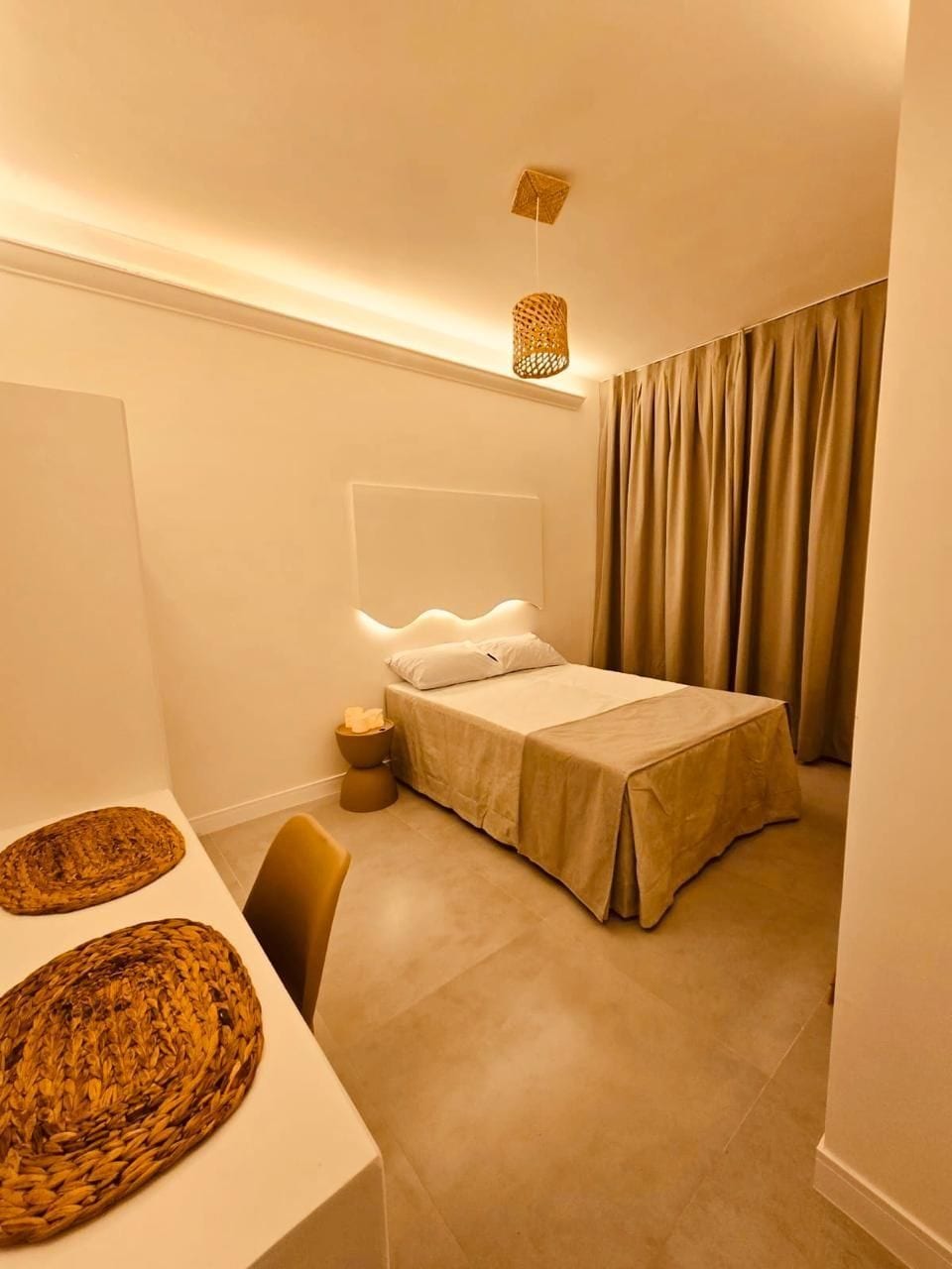 A bedroom with a bed, bedside tables, a hanging light fixture, and a curtain.